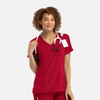 A mock wrap top in a vibrant red colour, featuring a v-neck design and a logo, worn by a smiling model with a stethoscope.