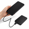 A black solid state power bank with a charging cable connected, held in a hand.