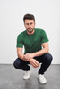A green T-shirt worn by a man squatting in jeans and white sneakers, featuring a logo.