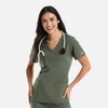 A woman wearing a green double V-neck top with a stethoscope around her neck and pockets. The top has a logo.