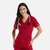 A woman wearing a red double V-neck top with a stethoscope around her neck, smiling and standing with hands on her hips.