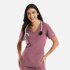 A woman in a pink double V-neck top wearing a stethoscope, with two pockets visible. The top has a logo.