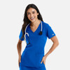 A woman in a bright blue, short-sleeved double V-neck top with a stethoscope around her neck, smiling.