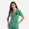 A woman smiles wearing a green double V-neck top, paired with a stethoscope around her neck. The top has pockets.