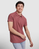 A young man in a burgundy polo shirt is smiling while posing against a neutral background. The shirt features a logo.