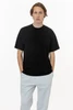 A black short sleeve crewneck t-shirt worn by a model, paired with light grey pants. The t-shirt features a logo.