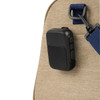 A black magnetic Bluetooth speaker attached to a tan bag strap. The speaker features buttons and a sleek design.