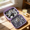 A portable mini suitcase in lavender, filled with various containers, accessories, and a mesh pocket, resting on a wooden table.