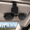 A black visor glasses holder mounted on a car's sun visor, holding a pair of silver sunglasses.