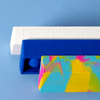 Three popper rulers in vibrant colours: a white ruler, a blue ruler, and a multicoloured patterned ruler, stacked together.