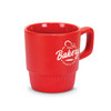 A red stackable coffee mug with a textured base and a logo featuring baking-related imagery.