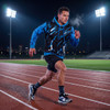 A man in a black and blue active hoodie runs on a track under stadium lights, wearing shorts and athletic socks.