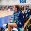 A custom women's active hoodie in blue and teal with a geometric pattern, worn by a seated athlete on the sidelines.