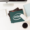 A green fabric mouse mat with a logo, placed on a desk alongside a white mouse, coffee cup, and notebook.
