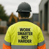 A worker in a high-visibility yellow jacket and hard hat, facing away, on a construction site.