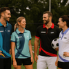 A group of five individuals wearing polo shirts in various colours, featuring logos, and standing on a sports field.