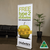 A roll-up banner featuring an apple and a measuring tape, predominantly white with green accents, and an Australian made logo.