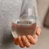 A stemless, shatterproof white wine glass in a hand, featuring a logo and containing a light beverage.