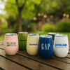 A collection of plastic cups and tumblers in various colours, featuring different logos and designs, on a wooden surface.