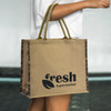 A jute tote bag in natural brown with dark patterned sides and a logo on one side.