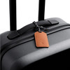 A black suitcase with a brown leather luggage tag attached, featuring a braided string for fastening.