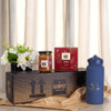 A blue drink bottle, a jar of jam, a box of biscuits, and a vase of flowers arranged on a decorative box.