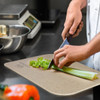 A chopping board in a neutral colour with celery being chopped, featuring a person's hand and a knife.