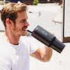 A drink bottle, the Rhino 1.2L Tumbler, in black with a sipping straw, held by a man outdoors.