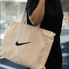 A large cream tote bag with a black logo being held by a person.