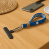 A blue wristlet with a T-shaped clip and a carabiner, resting on a wooden table next to a phone.