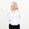 A white women's shirt with long sleeves and a button-up front, worn with black trousers. The model stands facing sideways.