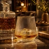 A drink glass with a ridged texture, filled with amber liquid, sits on a marble surface beside a crystal decanter.