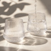 A drink bottle featuring a ribbed design, made of clear glass, with water being poured into two glasses.