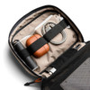 A tech kit featuring a grey exterior, tan interior, drink bottle, earphones, charging cables, and a pen.