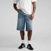 A pair of blue denim shorts featuring a relaxed fit, worn by a person with tattoos and black sneakers.