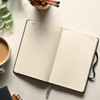 An open dark blue Moleskine 2027 planner with lined pages, surrounded by a coffee cup and stationery.