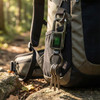 A black and green Smart Tag Bluetooth Tracker attached to a backpack, with keys hanging from it in a forest setting.