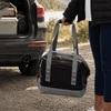 A foldable cooler in black and grey, held by a person near the back of a vehicle. It has carrying straps and a logo.