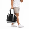A foldable cooler in black and silver, carried by a person in shorts and a white shirt, with a logo visible.