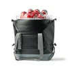 A foldable cooler in black, filled with ice and red cans of cola, featuring shoulder straps and a logo.