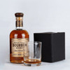 A bourbon whiskey bottle with a wooden cap, a rocks glass beside it, and a black box in the background.