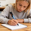 A child writing in a notebook with a black and blue stylus pen on a wooden table.