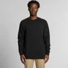 A black jumper is worn by a model with short, curly hair against a neutral background. The garment has a simple design and a logo.