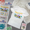 A white t-shirt featuring a colourful design with beach elements and logos, arranged on a flat surface.