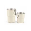 A stainless steel camping mug set in cream, featuring a handle, includes a larger and a smaller mug.
