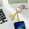A custom-shaped PVC charging cable in yellow with a bunny keyring, resting on a desk next to a laptop and smartphone.
