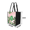 A tall non-woven tote bag featuring a floral design in pink and green, with black sides and handles.