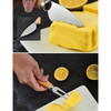 A butter knife with a wooden handle cutting through yellow butter, surrounded by halved lemons on a dark surface.
