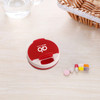 A round, red and cream pill box with a hinged lid, alongside assorted pills on a wooden surface.