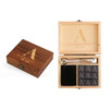 A wooden box featuring a logo, containing nine black whiskey stones and two stirring utensils.